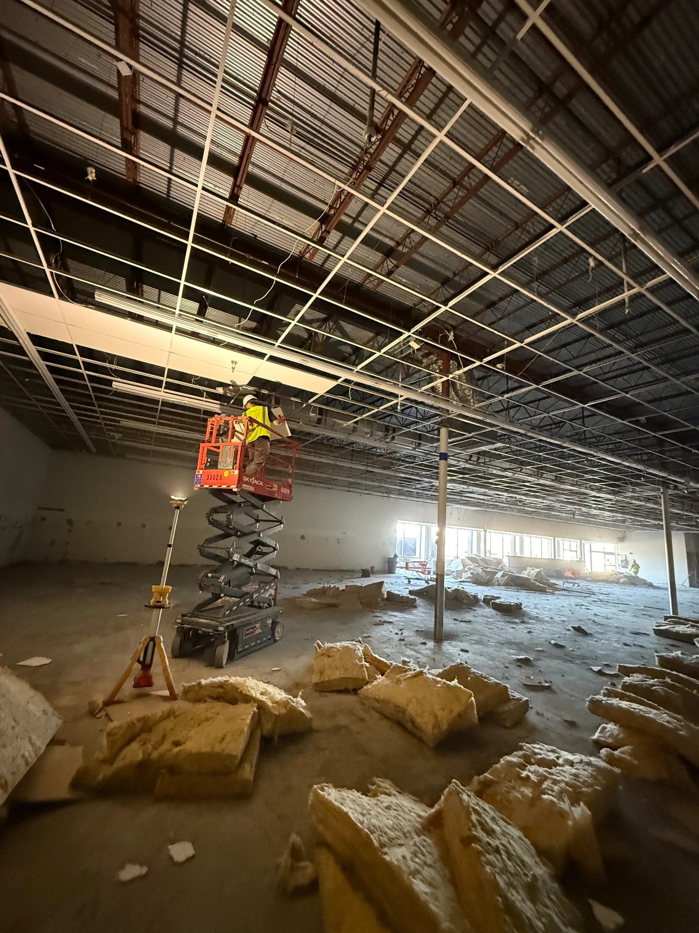 Commercial ceiling demolition with worker on scissor lift removing grid and insulation